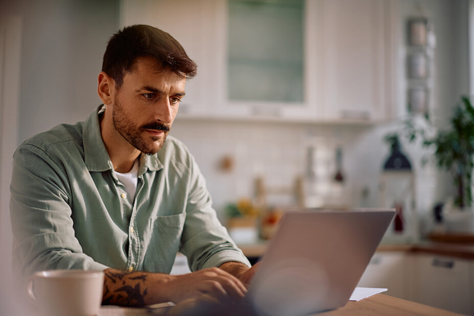 Mid adult man typing an email on laptop while working at home