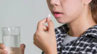 A woman takes a pill with a glass of water