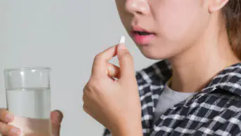 A woman takes a pill with a glass of water