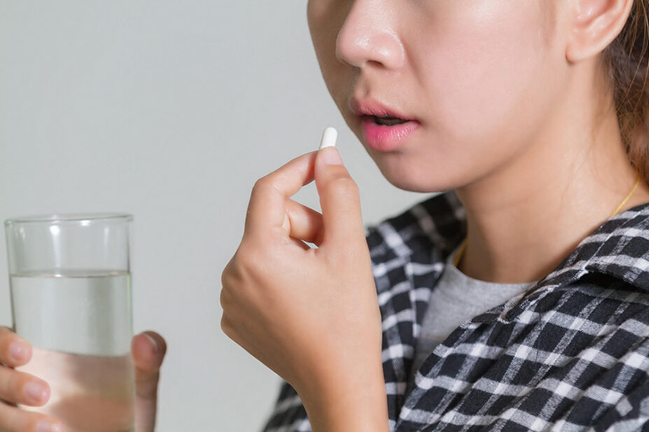 A woman takes a pill with a glass of water