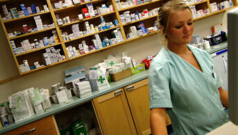 A pharmacist works on a computer in a community pharmacy
