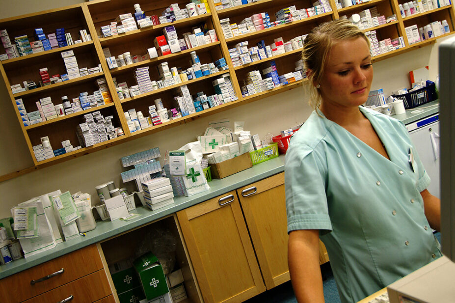 A pharmacist works on a computer in a community pharmacy