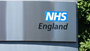 NHS England sign on grey surface with greenery in background