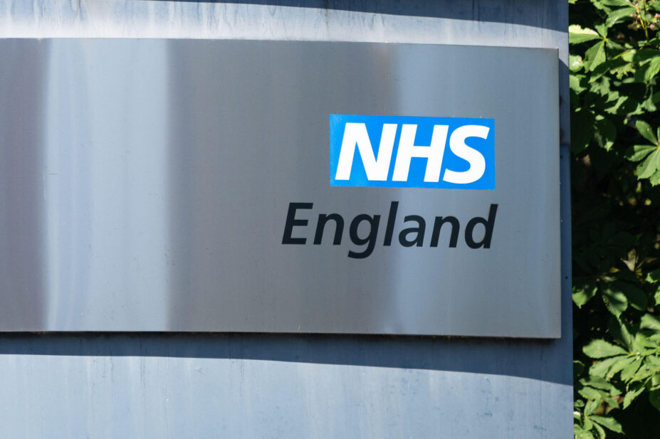 NHS England sign on grey surface with greenery in background