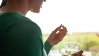 A woman takes a pill with a glass of water