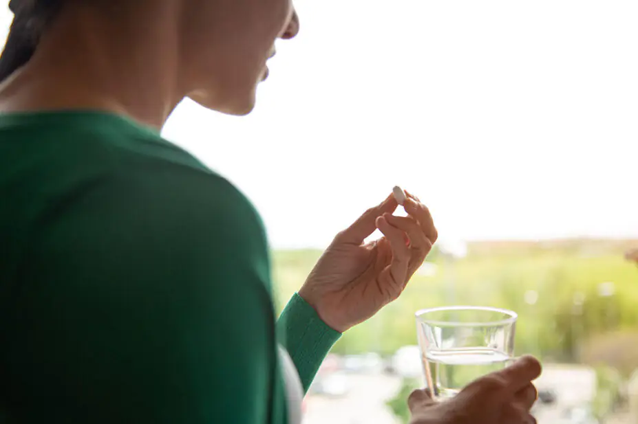 A woman takes a pill with a glass of water