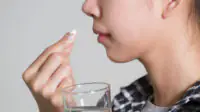 A woman takes medication with a glass of water