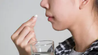 A woman takes medication with a glass of water