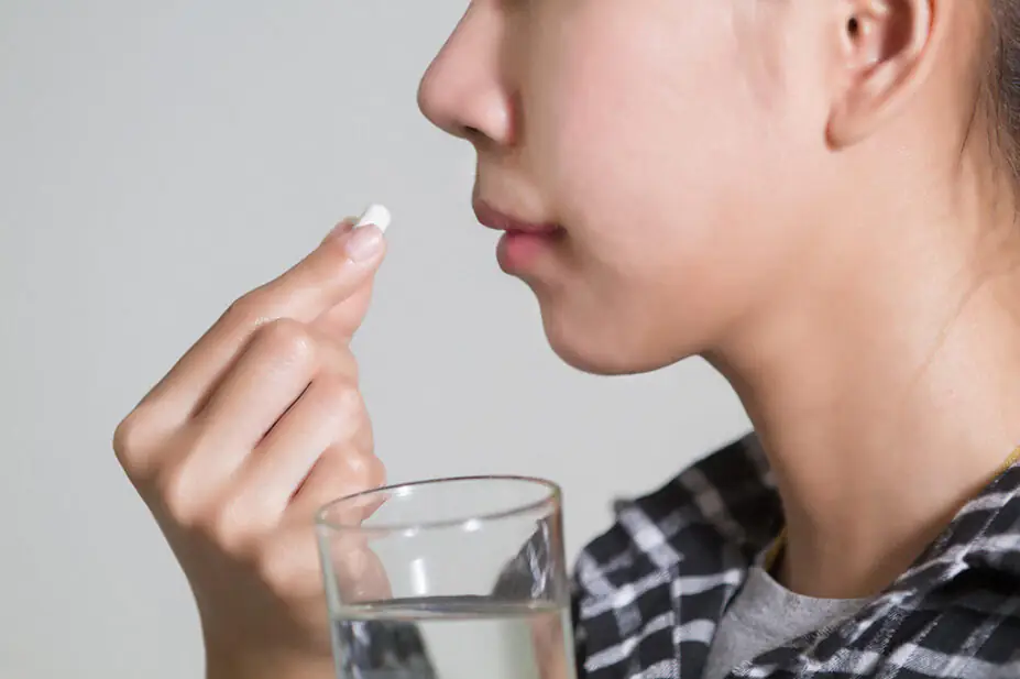 A woman takes medication with a glass of water