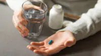 Man's hands holds a blue capsule and glass of water