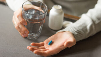 Man's hands holds a blue capsule and glass of water