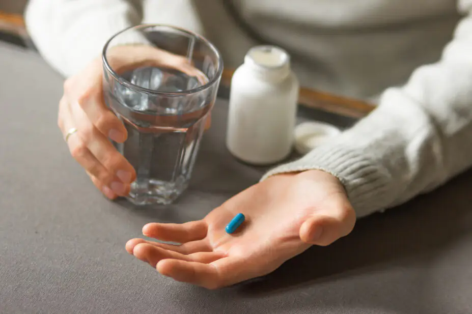 Man's hands holds a blue capsule and glass of water