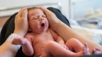 A newborn on the lap of its mother in hospital, showing hospital wrist band