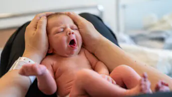 A newborn on the lap of its mother in hospital, showing hospital wrist band