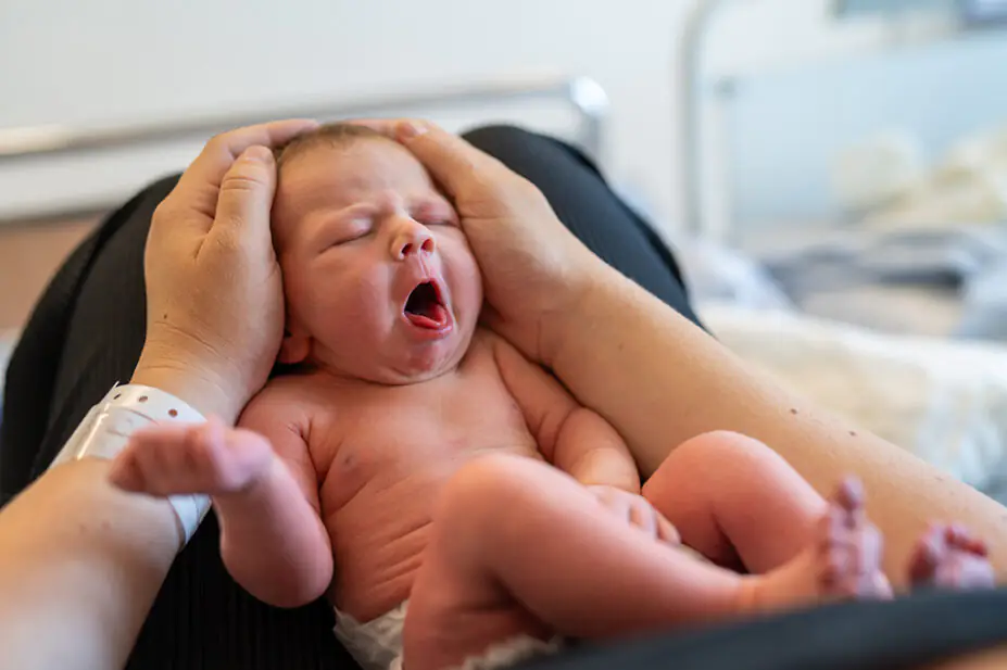 A newborn on the lap of its mother in hospital, showing hospital wrist band