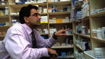 A pharmacist looks at a shelf of medicines