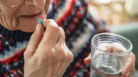 An elderly woman takes medication with a glass of water