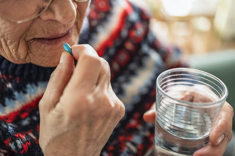 An elderly woman takes medication with a glass of water