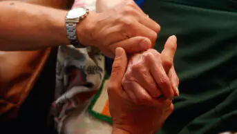 A loved one holds the hand of a patient in palliative care