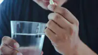 A man takes a tablet with a glass of water