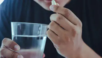 A man takes a tablet with a glass of water