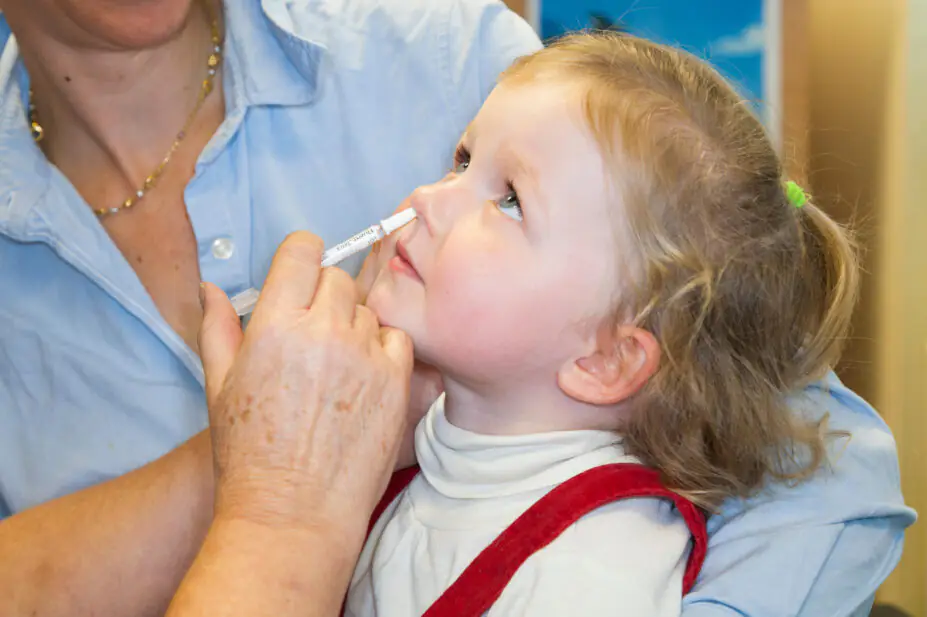 2 year old child, with her mum / mother, receives dose of Fluenz flu vaccine nasal spray immunisation from NHS Practice nurse UK