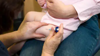 C2F74W MMR etc immunisation / inoculation / jab / from a syringe into a one year old / 12 13 twelve thirteen month baby's thigh / leg.