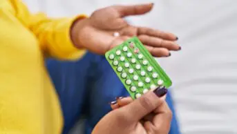 African american woman holding birth control pills sitting on bed at bedroom