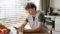 Diabetic teen boy checking his phone, sitting in kitchen.