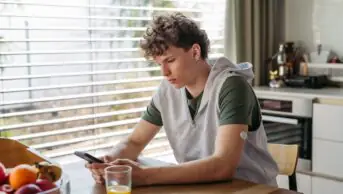 Diabetic teen boy checking his phone, sitting in kitchen.