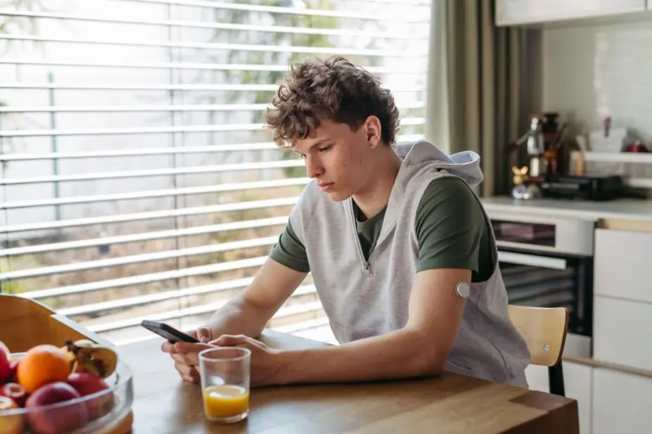 Diabetic teen boy checking his phone, sitting in kitchen.