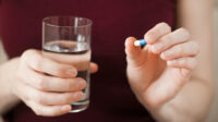 A woman takes a tablet with a glass of water