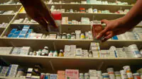 Customers reach for medicines on a shelf in a community pharmacy