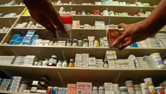 Customers reach for medicines on a shelf in a community pharmacy