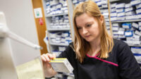 A pharmacist checks a box of medicine in a community pharmacy