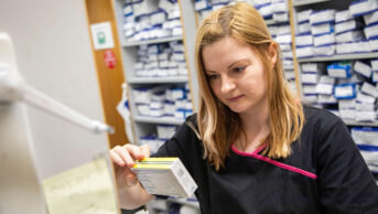 A pharmacist checks a box of medicine in a community pharmacy