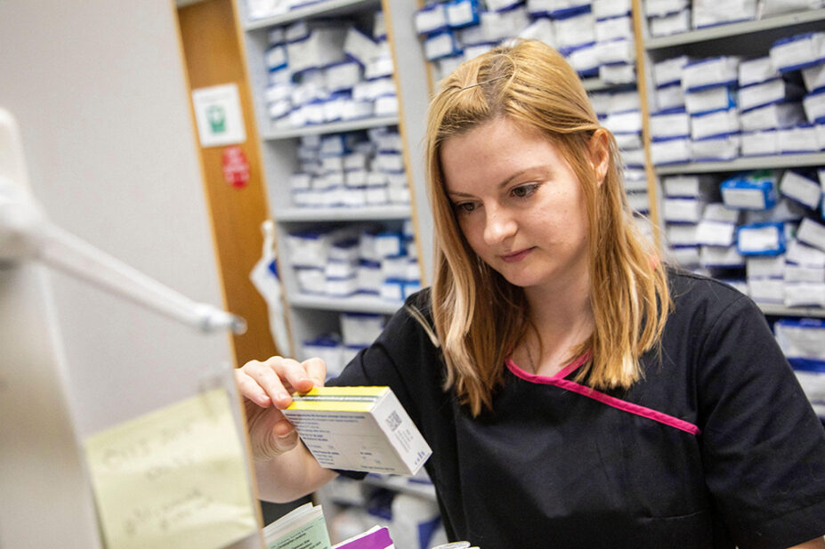 A pharmacist checks a box of medicine in a community pharmacy