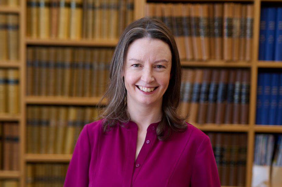 Geraldine standing against wooden bookshelf wearing dark pink shirt