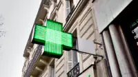 A green cross sign outside of a community pharmacy