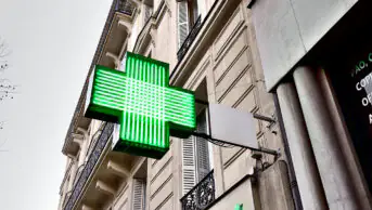 A green cross sign outside of a community pharmacy