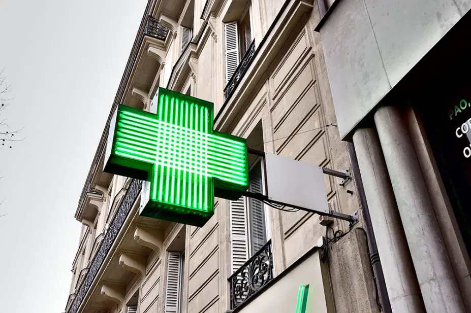 A green cross sign outside of a community pharmacy