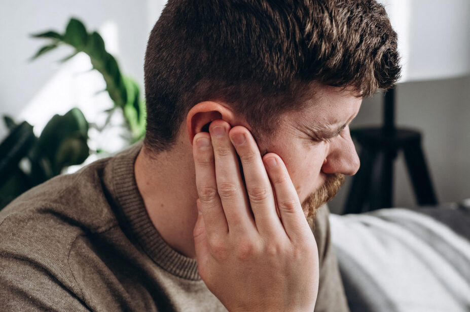 Close-up of unhealthy young caucasian man 30s touching ear, suffering from sudden throbbing