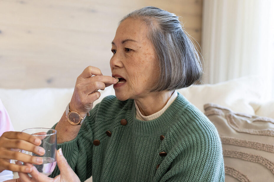 An older woman takes medication with a glass of water