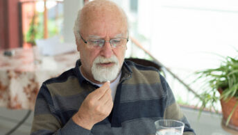 An older man takes a tablet with a glass of water