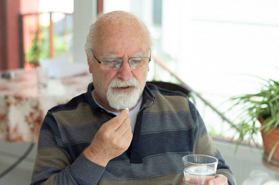 An older man takes a tablet with a glass of water