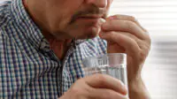A middle aged man takes a tablet with water