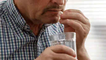 A middle aged man takes a tablet with water