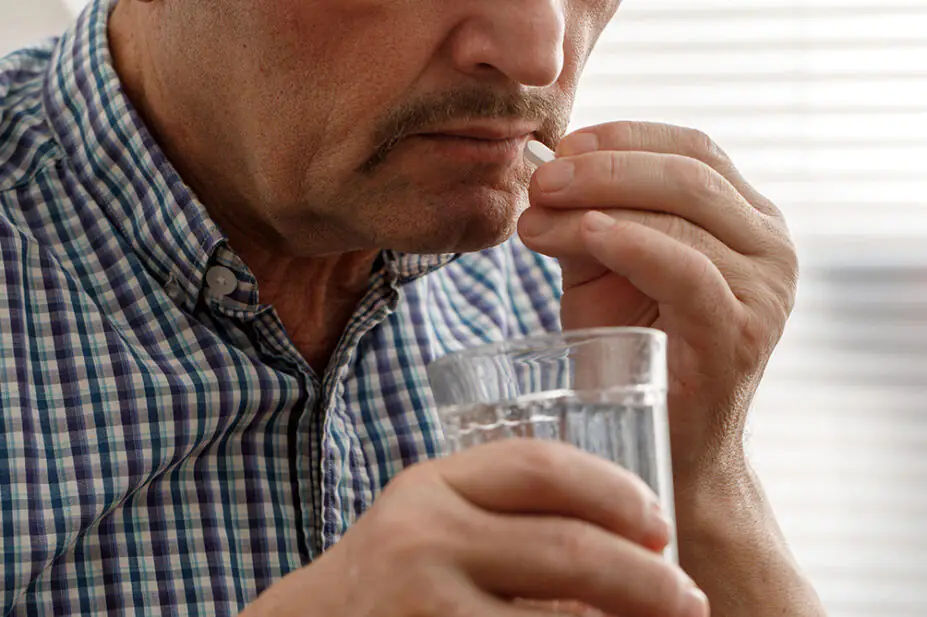 A middle aged man takes a tablet with water