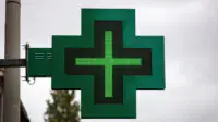 A green cross sign outside of a community pharmacy