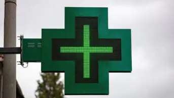 A green cross sign outside of a community pharmacy